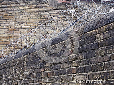 Coiled barbed razor wire running along the top of an old stone wall surrounding a building Stock Photo