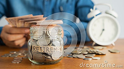A coin in a glass bottle Image blurred background of business people sitting counting money and a retro white alarm clock, Stock Photo