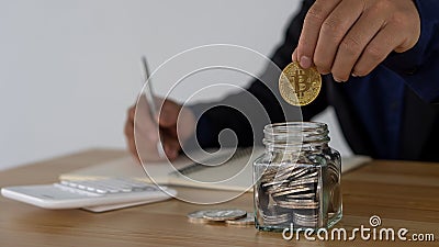 Coin-operated hand put a glass piggy bank on a businessman`s desk in an office with a calculator next to Stock Photo