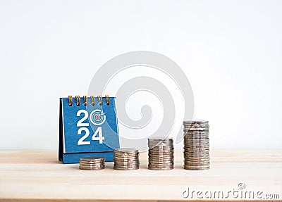 Coin stack as a growth graph with up arrows near 2024 desk calendar on wooden table and white background. Stock Photo
