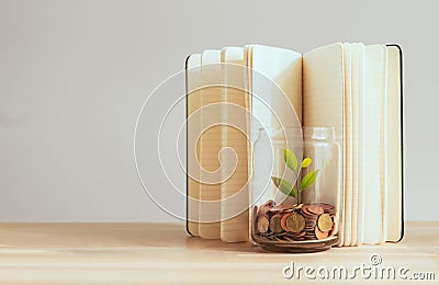 Coins in a bottle and the green tree with book background on the table, Financial planning for future expenditures. Stock Photo