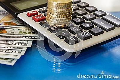 Coins on a calculator and dollars on a blue reflective background. Close-up. Stock Photo