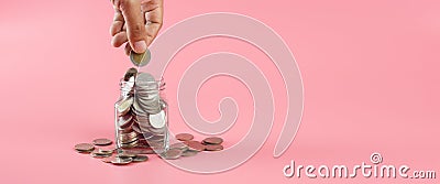 Coins in glass bottle put on table with hand putting money coins pink background, growth save or investment concept Stock Photo