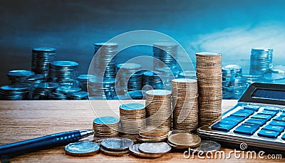 Coins stacked on a wooden desk with a pen and calculator. Concept of business and finance Stock Photo