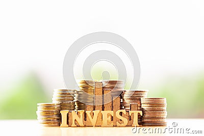 Coins stacking and Wooden Blocks with the text INVEST on greenery nature background. Stock Photo