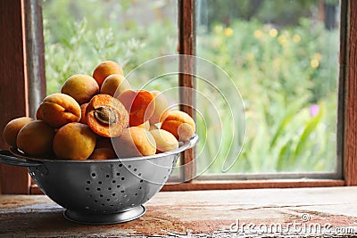 Colander with delicious ripe apricots on wooden table near window. Space for text Stock Photo