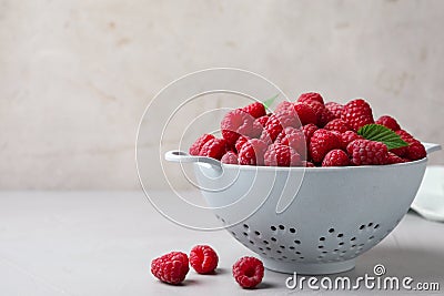Colander with delicious ripe raspberries on table against light background, space for text Stock Photo