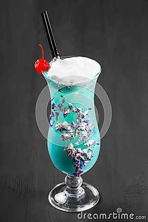 Cold alcoholic blue cocktail, decorated with berries and flowers in glass on black wooden background Stock Photo