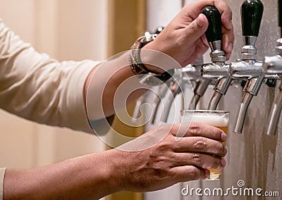 Cold draft beer poured into glass from silver beer dispenser, selective focus Stock Photo