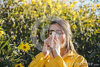 Cold flu season, runny nose. Flowering trees in background. Young girl sneezing and holding paper tissue in one hand and Stock Photo
