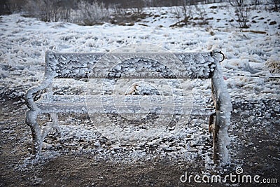 Cold winter photography image of outdoor bench or seat covered in wind swept frozen water and ice with snow background Stock Photo