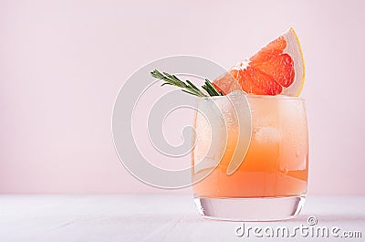 Cold fresh homemade grapefruit cocktail with ice, rosemary and pieces citrus on pastel pink background. Stock Photo
