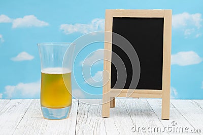 Cold glass of beer with chalkboard on weathered wood with clear sky Stock Photo