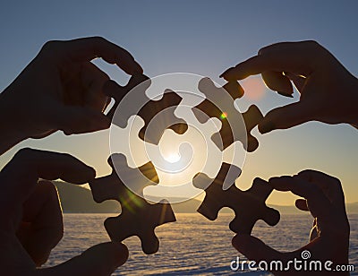 Collaborate four hands trying to connect a puzzle piece with a sunset background. Stock Photo