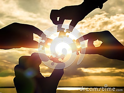 Collaborate four hands trying to connect a puzzle piece with a sunset background. Stock Photo