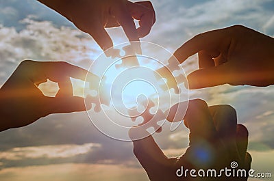 Collaborate four hands trying to connect a puzzle piece with a sunset background. Stock Photo