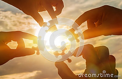 Collaborate four hands trying to connect a puzzle piece with a sunset background. A puzzle in hand against sunlight. Stock Photo