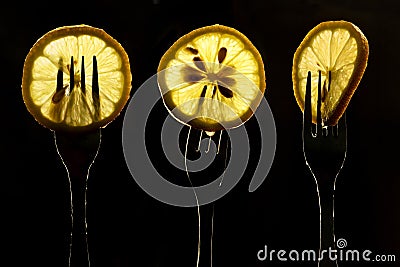 Collage of three slices of lemons on the fork on dark black background. silhouette of a fork in the back light. Drops of juice Stock Photo