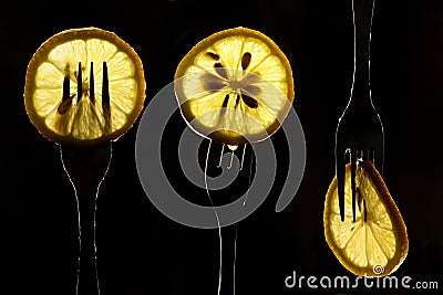 Collage of three slices of lemons on the fork on dark black background. silhouette of a fork in the back light. Drops of juice Stock Photo