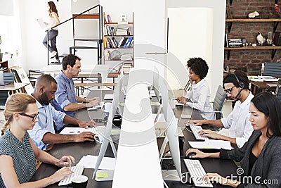 Colleagues sit using computers in a busy open plan office Stock Photo