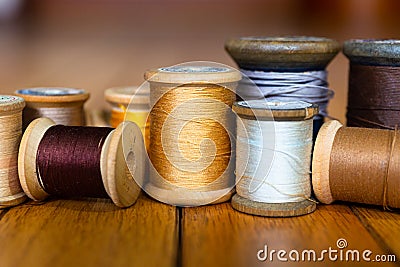 Black, Cream, Yellow, Gold, White, Silver, Dark Grey, and Beige Threads on Wooden Spools On Several Planks of Light Wood Stock Photo