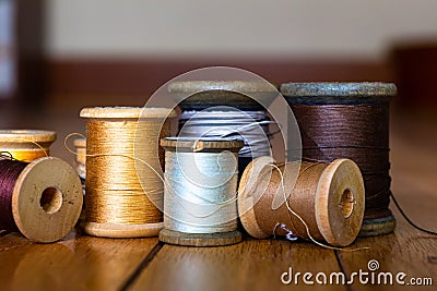 Black, Yellow, Gold, White, Silver, Dark Grey, and Beige Threads on Wooden Spools On Several Planks of Light Wood Stock Photo