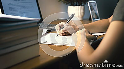 College or university student doing school homework at home. Working late at night. Young woman writing on paper with pen. Stock Photo