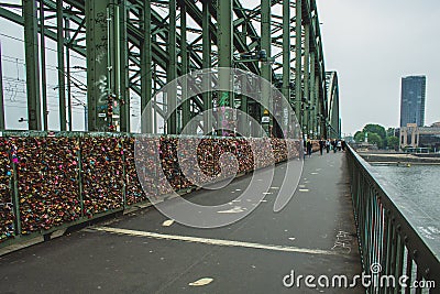 COLOGNE, GERMANY - May 20 2019 : Famous love padlocks hanging at Hohenzollern Bridge in Cologne. People walking on the bridge to Editorial Stock Photo