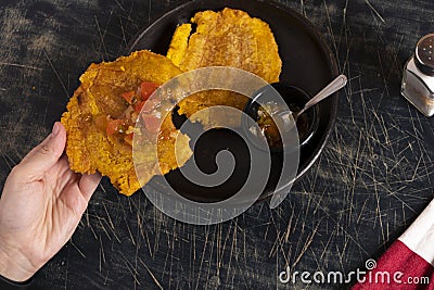 Colombian patacones dish with tomato sauce and onion hogao. Person eating traditional Latin dish. Banished trodden banana Stock Photo