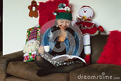 Colombian woman at Christmas sitting on the sofa reading a book and drinking coffee Stock Photo