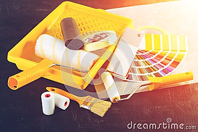 Color samples catalog, brush and paint rollers, different painting tools on dark background in rays of the sun, toned image. Stock Photo