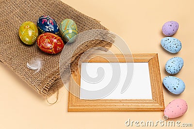 Easter eggs on a sackcloth bag and a frame on the beige background. Stock Photo