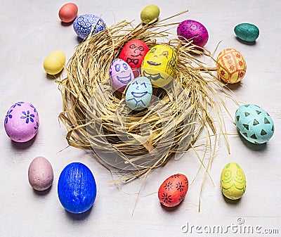 Colored ornamental eggs for Easter with painted faces lie in a nest wooden rustic background top view close up Stock Photo