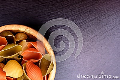 Colored pasta lie in a wooden cup on a black stone slate, place for text Stock Photo