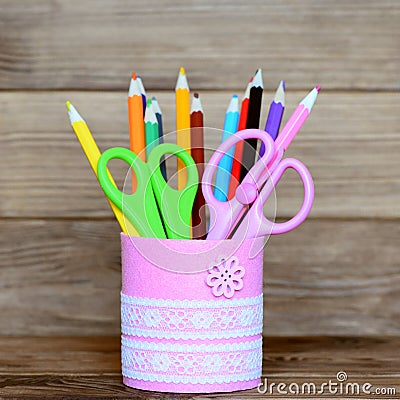 Colored pencils and scissors in a decorative jar. Recycled metal jar for storage of stationery on wooden background Stock Photo