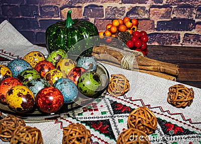 Colored quail eggs in a plate on a tablecloth with pumpkin, cinnamon and mountain ash Stock Photo
