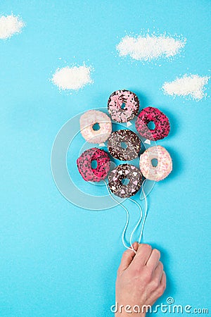 Mini donuts on blue background, creative food idea, hand holding donuts in a shape of balloons in the sky and sugar clouds Stock Photo