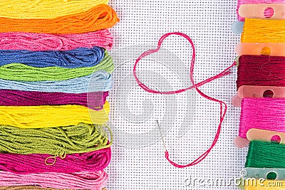 Colored thread for embroidery on white canvas, a needle with red thread in the shape of a heart. The concept of love for a hobby. Stock Photo