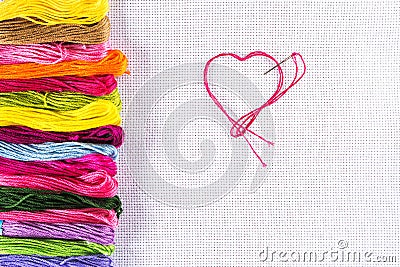 Colored thread for embroidery on white canvas, a needle with red thread in the shape of a heart. The concept of love for a hobby. Stock Photo