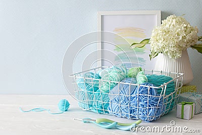 Colored yarn in cool shades lies in a white metal basket. Crochet hooks. Hydrangea in a vase in the Nordic style. Stock Photo