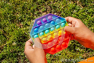 Colorful antistress sensory toy fidget push pop it in kid& x27;s hands. Pop it toy. Girl plays outside. Stock Photo
