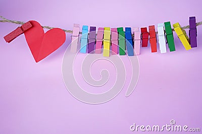 Red heart and colorful paper clips on rope on soft pink purple background. Stock Photo