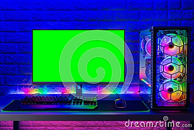 Colorful bright illuminated rgb gaming pc with keyboard mouse monitor with green screen copy space front of LED light brick stone Stock Photo