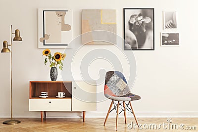 Colorful chair standing in white living room interior with gallery on wall, cupboard with flowers and tea cups Stock Photo