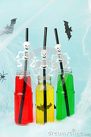 Colorful cocktails in glass bottles with skeleton straw on light blue background, Happy Halloween party banner, seasonal stylish Stock Photo