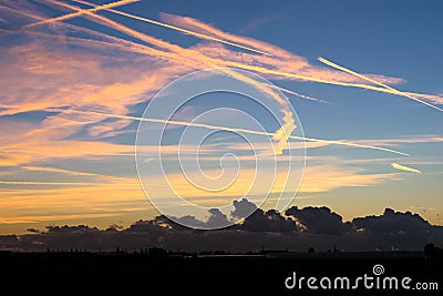Contrails high up in the sky are colorful illuminated by the light of the setting sun Stock Photo