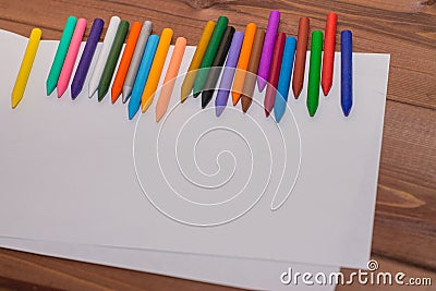 Colorful crayons with a white blank sheet of paper on a wooden b Stock Photo