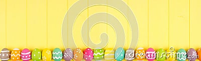 Colorful Easter banner with a row border of Easter Eggs over a yellow wood background with copy space Stock Photo