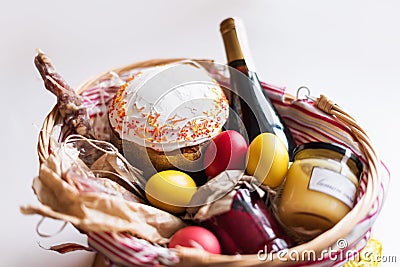 Colorful easter eggs in a basket with cake, red wine, hamon or jerky and dry smoked sausage on white background. Stock Photo