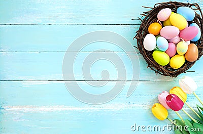 Colorful Easter eggs in nest with tulip flower on blue wooden background. Stock Photo